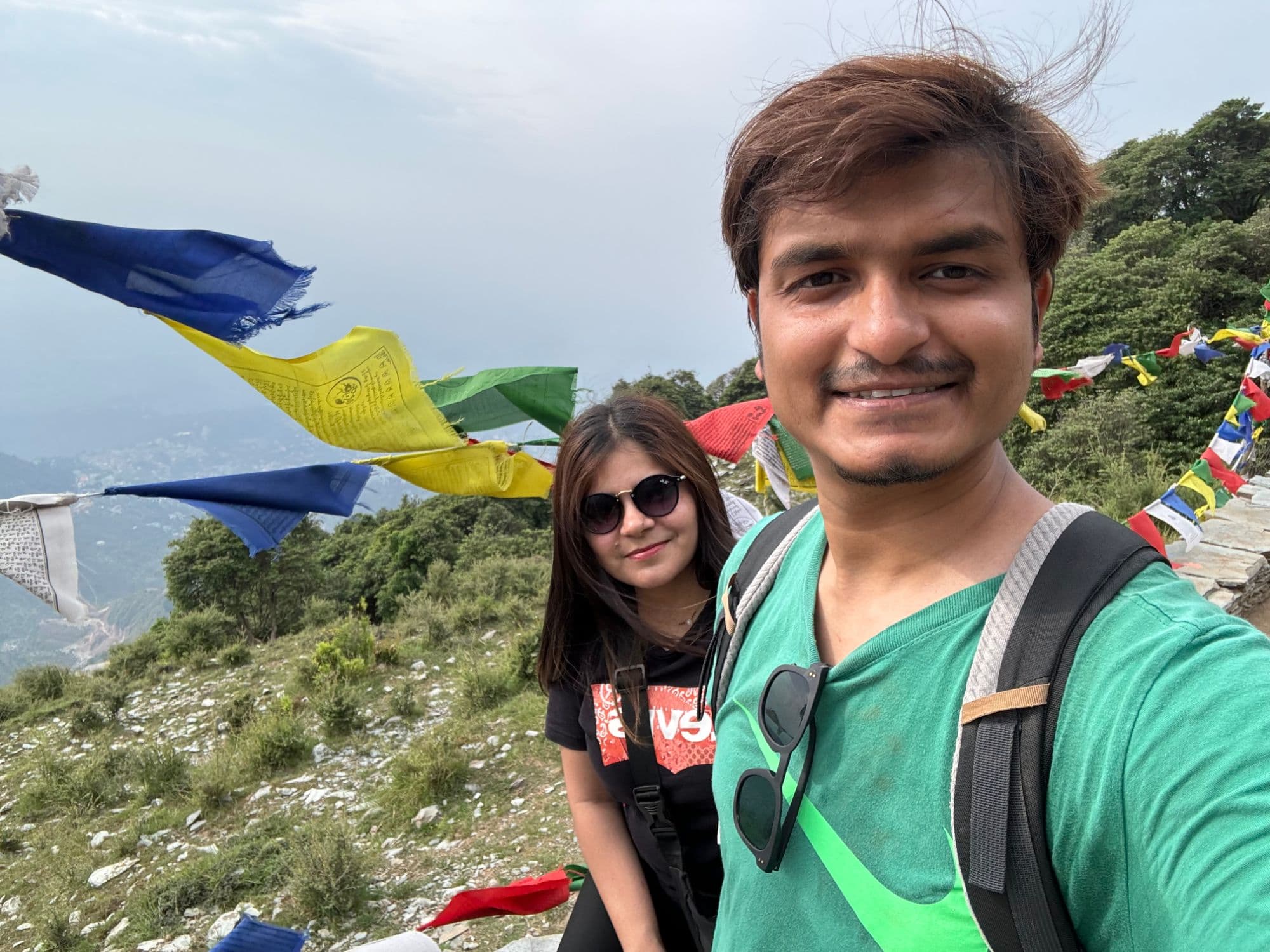 Aman and Shilpa on a hillside, prayer flags strung across the valley behind them